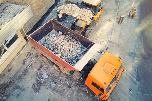 Bulldozer loader uploading waste and debris into dump truck at construction site. building dismantling and construction waste disposal service. Aerial drone industrial background.